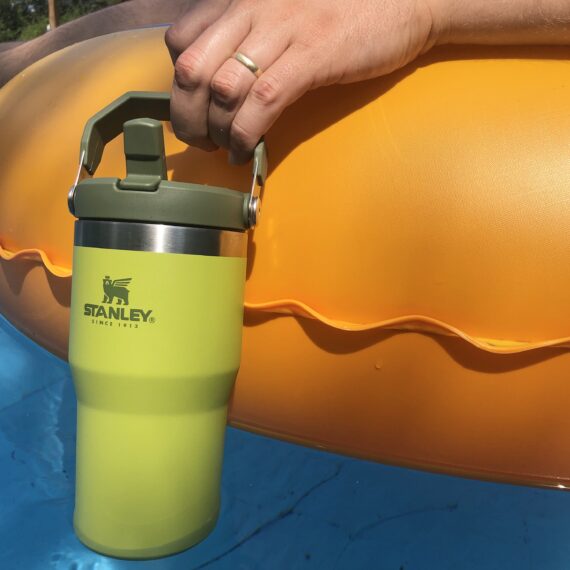 Stanley tumbler in hand hanging over the edge of a floatie in a pool